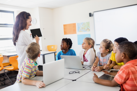 Image of teacher holding laptop surrounded by students