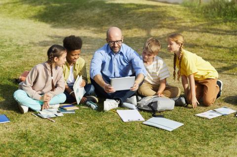 Image of a teacher on lawn surrounded by students